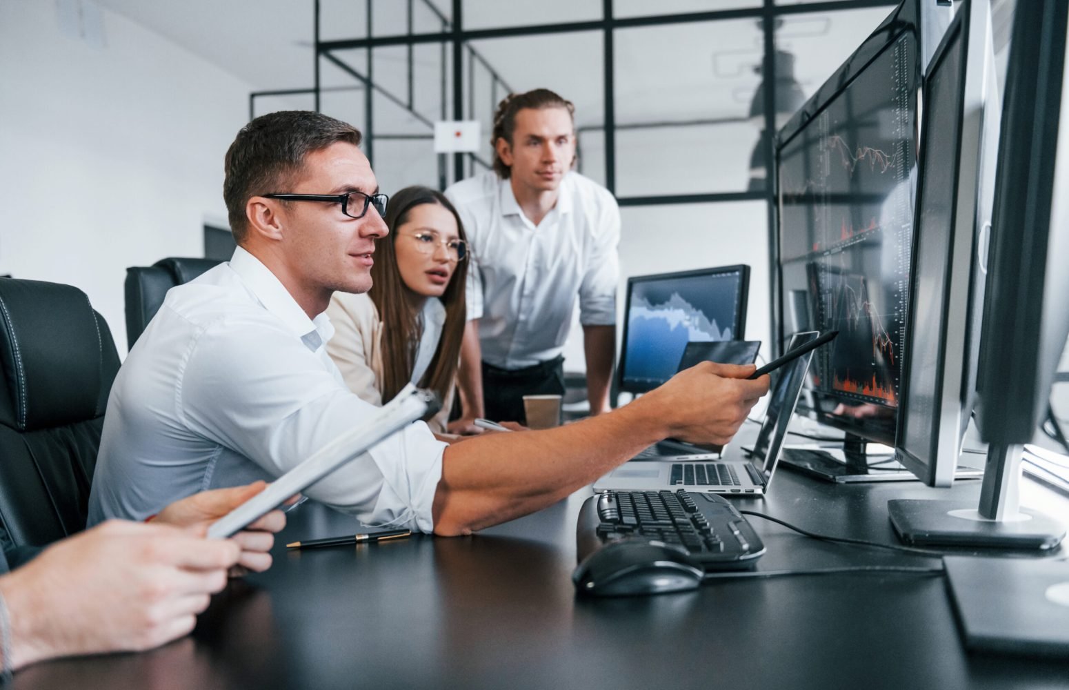 Sitting by the table. Team of stockbrokers works in modern office with many display screens.