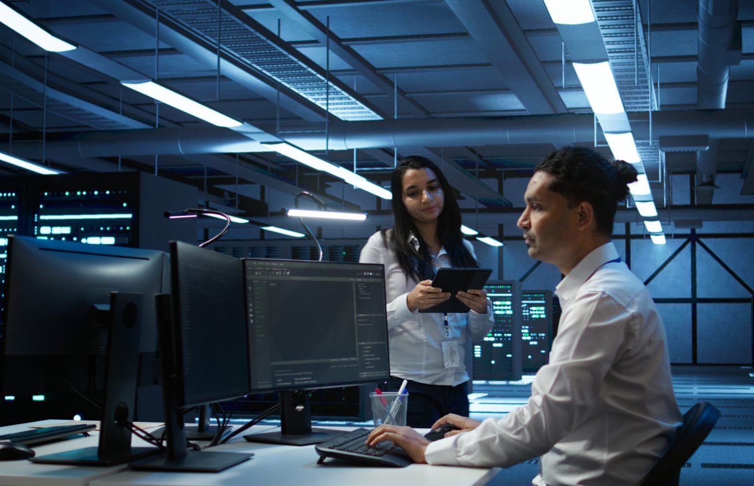 Team of programmers in high tech data center troubleshooting issues using tablet. Teamworking colleagues in server farm using device, establishing performance benchmarks, camera B